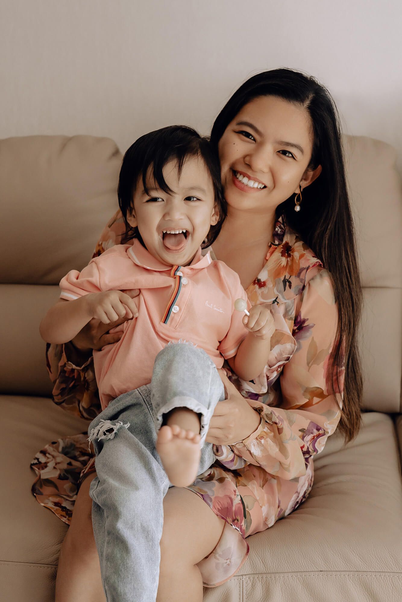 A joyful moment on a beige couch shows heartwarming interaction between parent and child wearing pink and floral outfits.