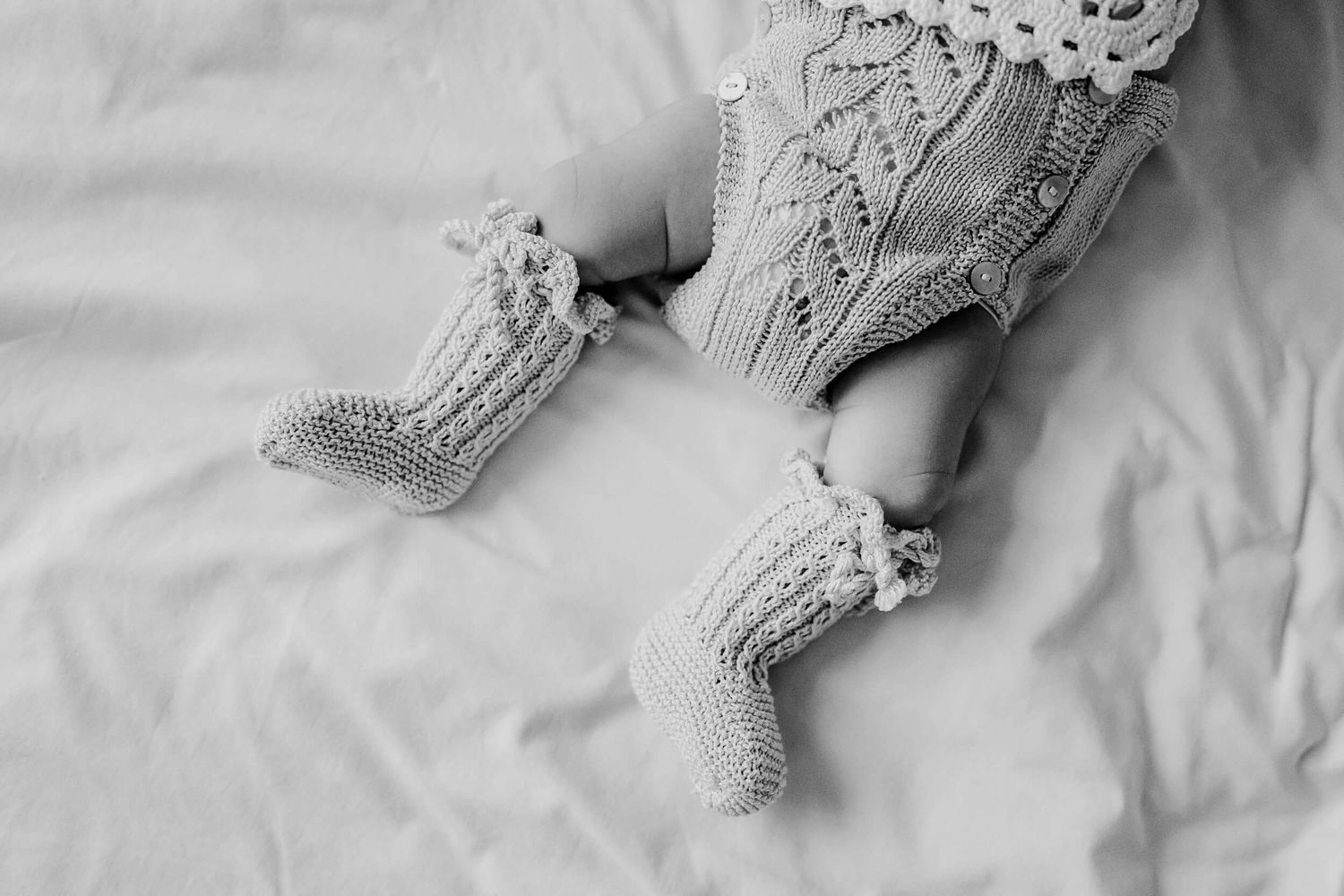 Soft focus view of lace details and newborn's feet on white sheets.