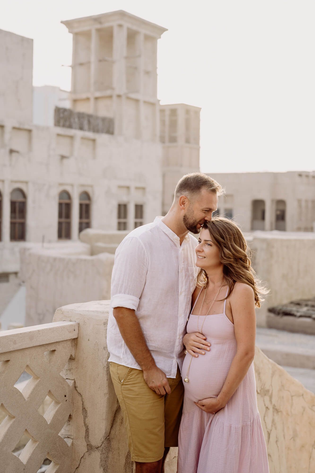 A romantic couple shares intimate moments against a white stone architectural backdrop in a series of candid photos.