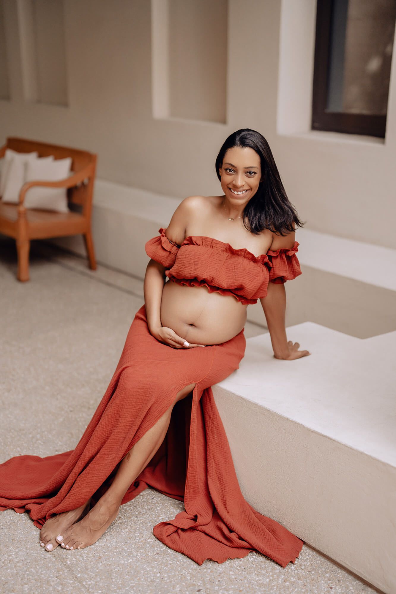 Elegant maternity portraits showing flowing rust-colored dress against minimalist interior.