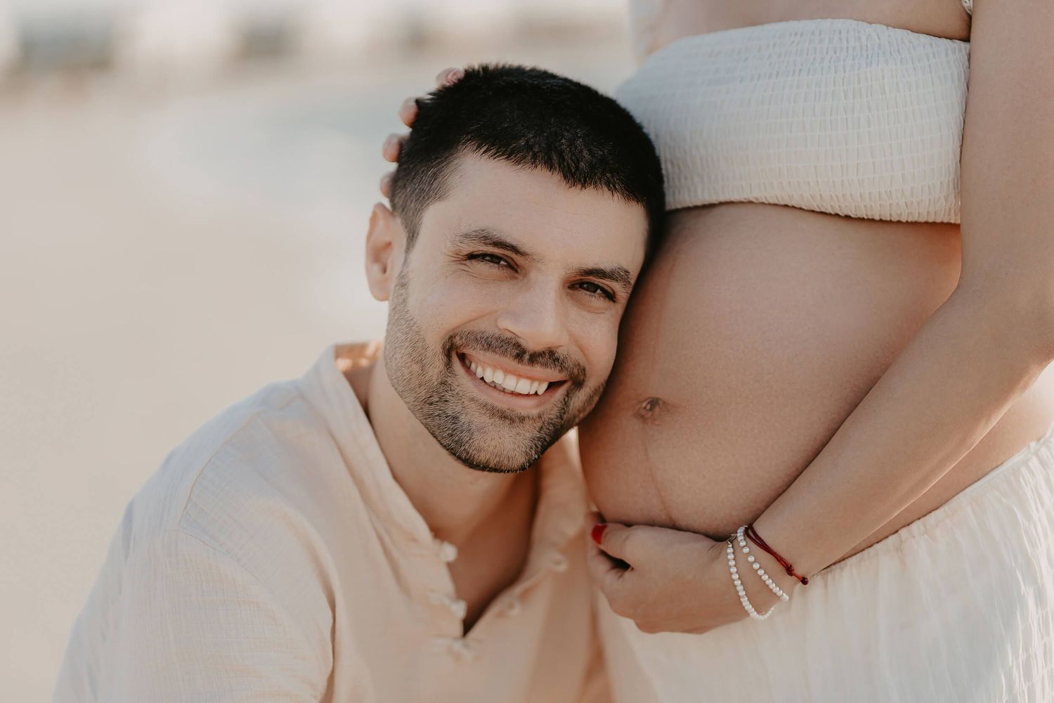 Intimate maternity photoshoot with someone gently resting their head against a pregnant belly outdoors in soft lighting.