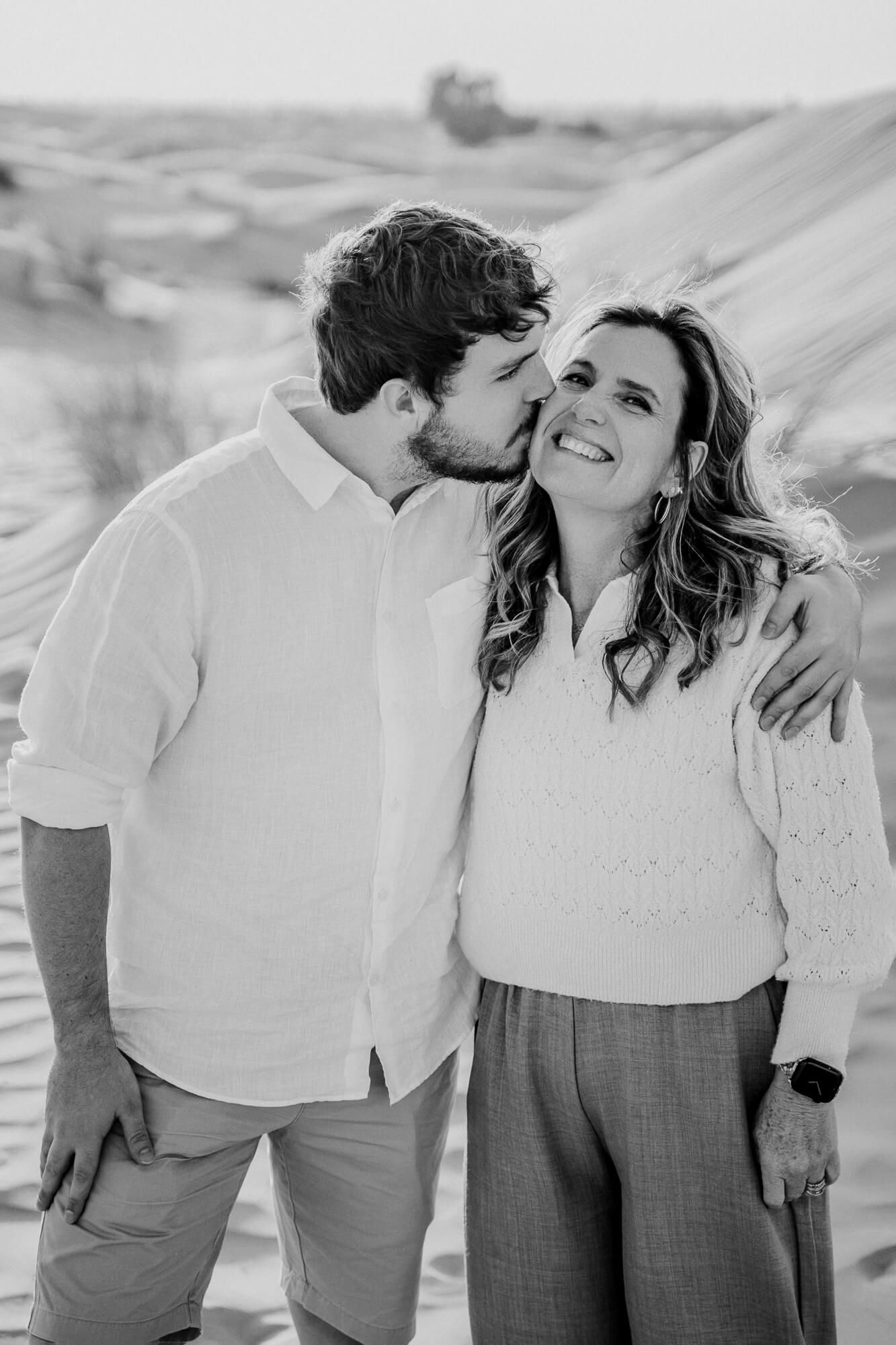Black and white intimate moment captured between a couple against a desert landscape backdrop.