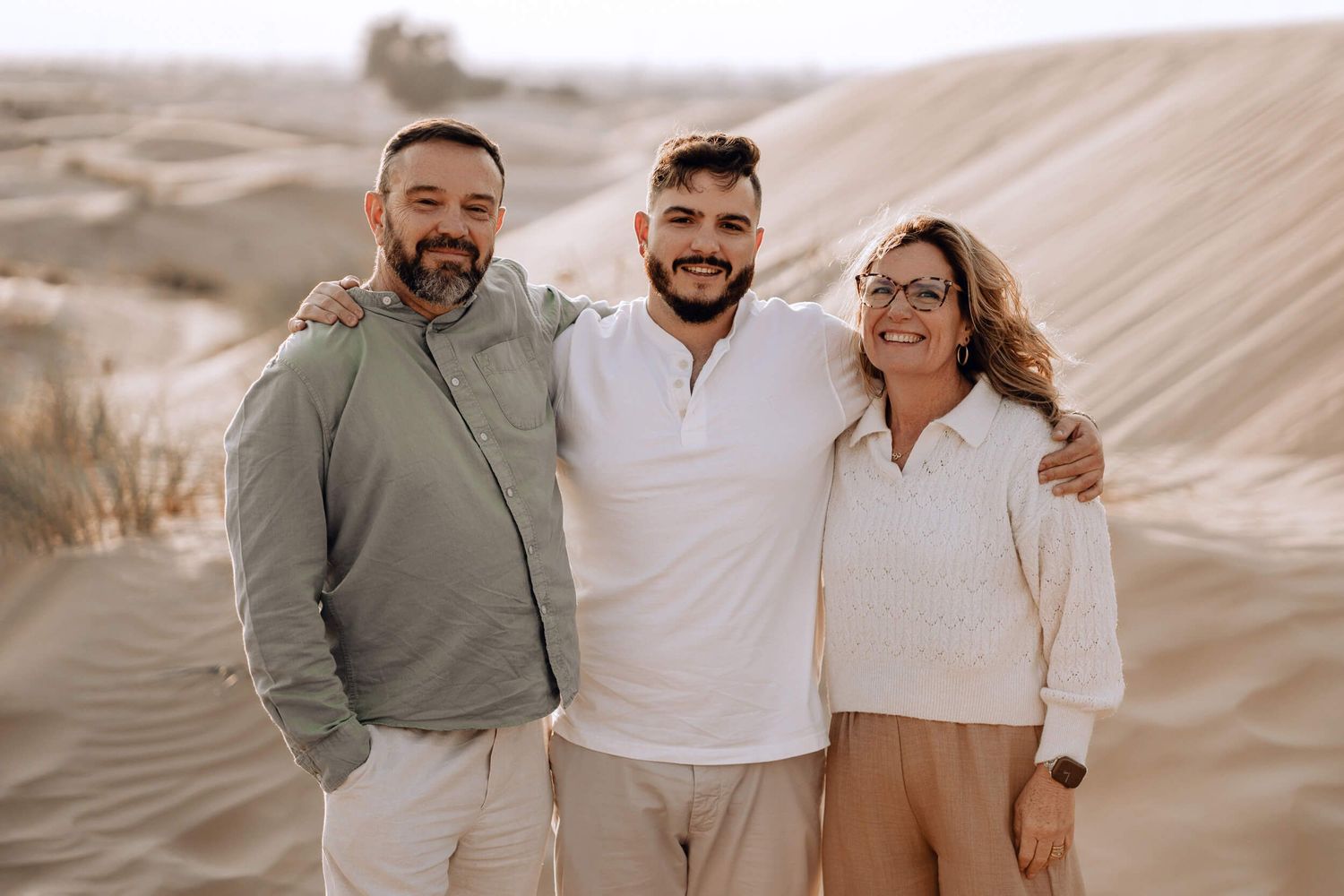 Family group smiling and embracing while standing together on desert sand dunes.