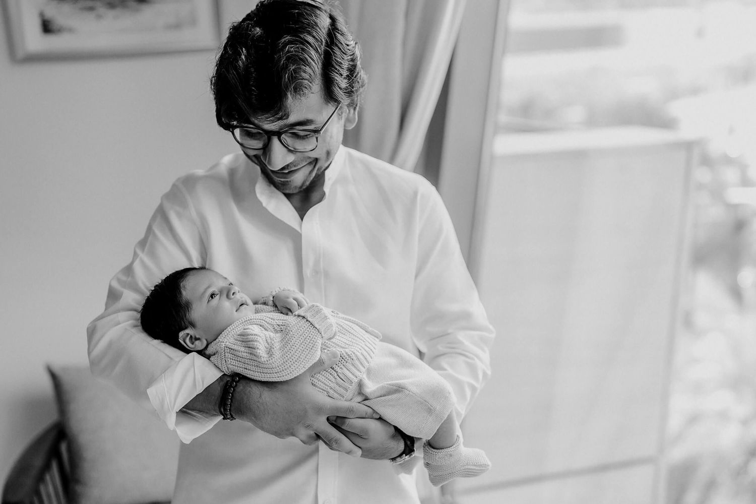 Parent in white shirt tenderly holding sleeping newborn baby in black and white portrait.