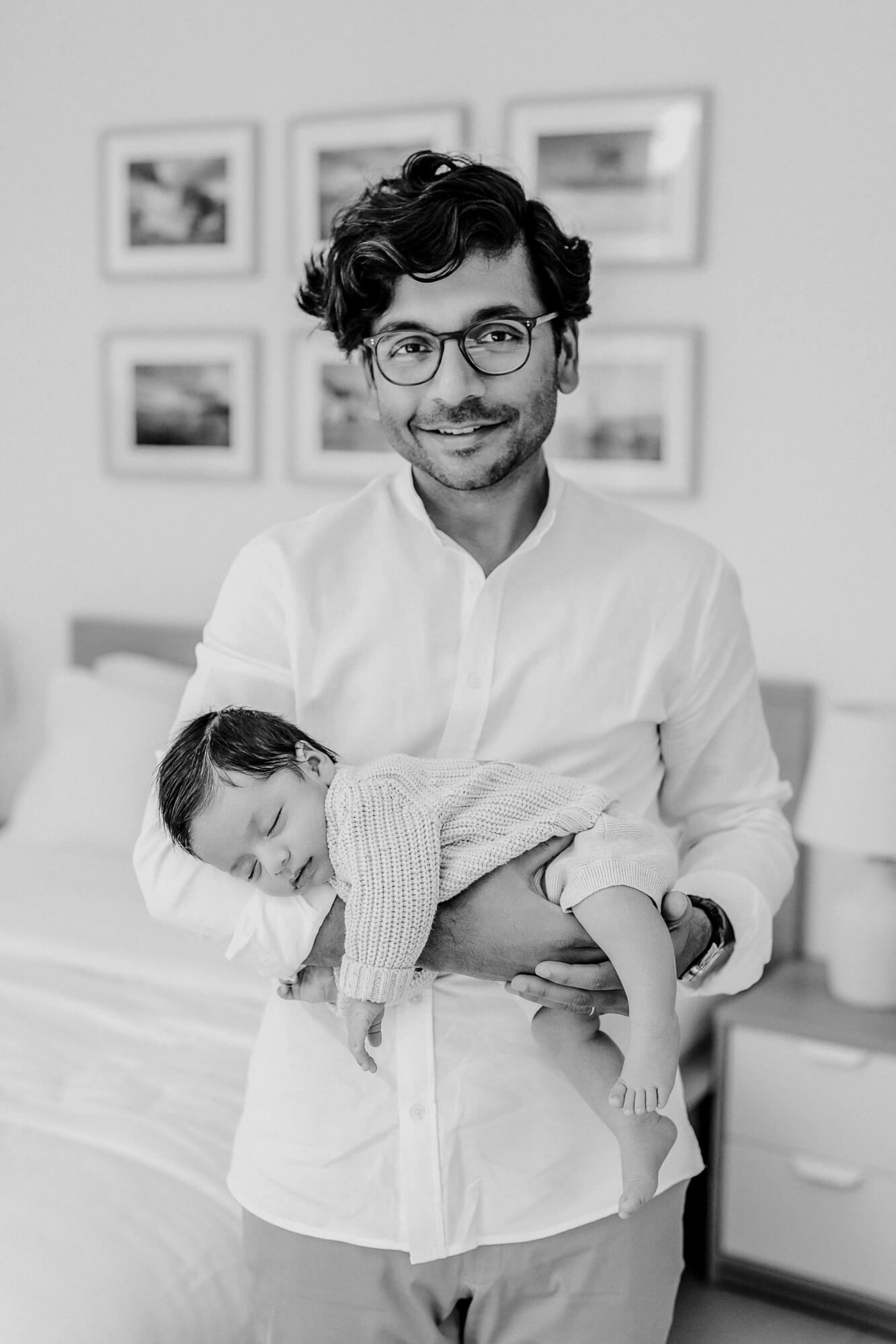 Person smiling while holding sleeping baby in cream knit sweater.
