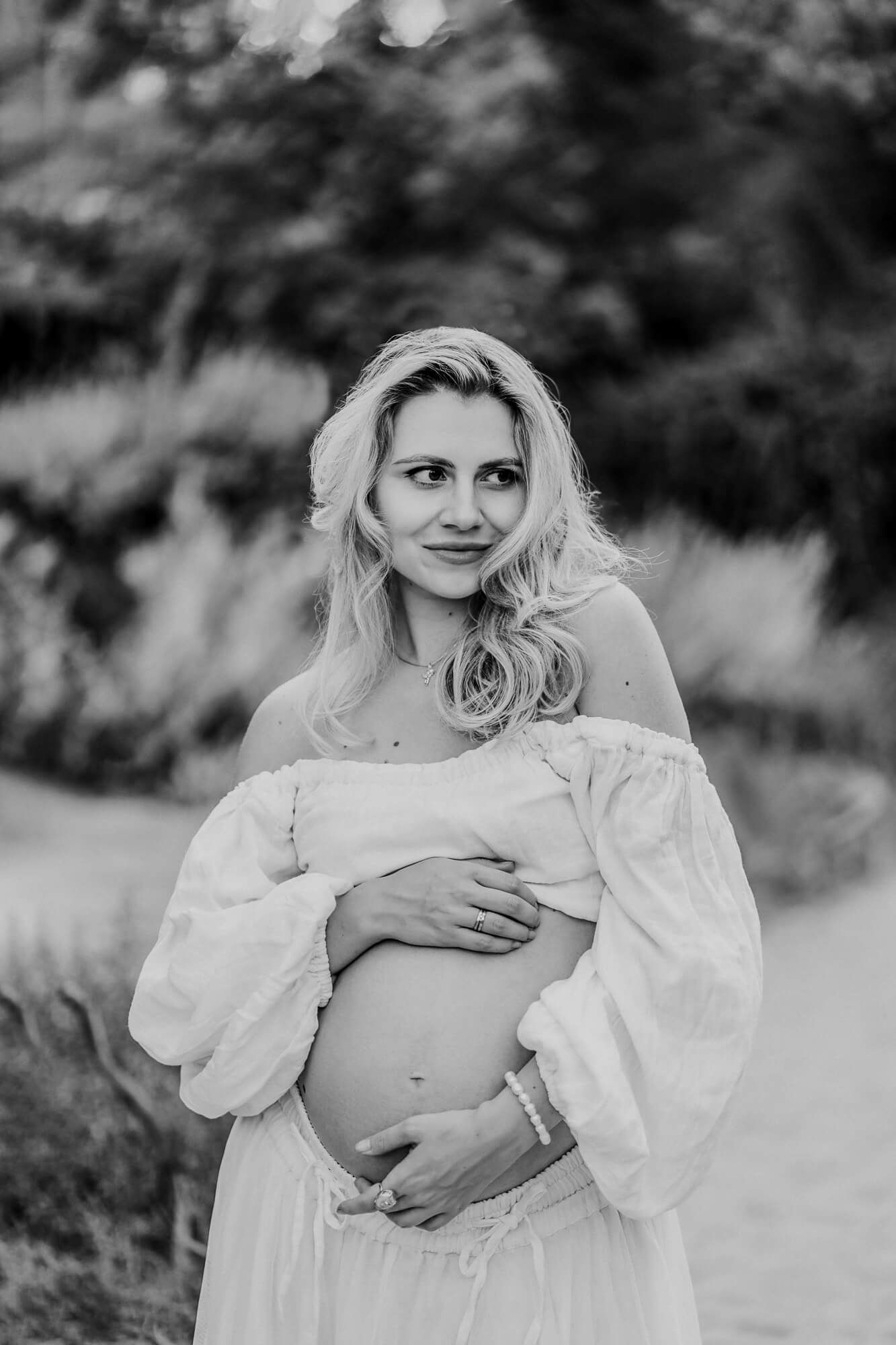 A black and white maternity portrait showing a gentle embrace of the baby bump in a white dress.