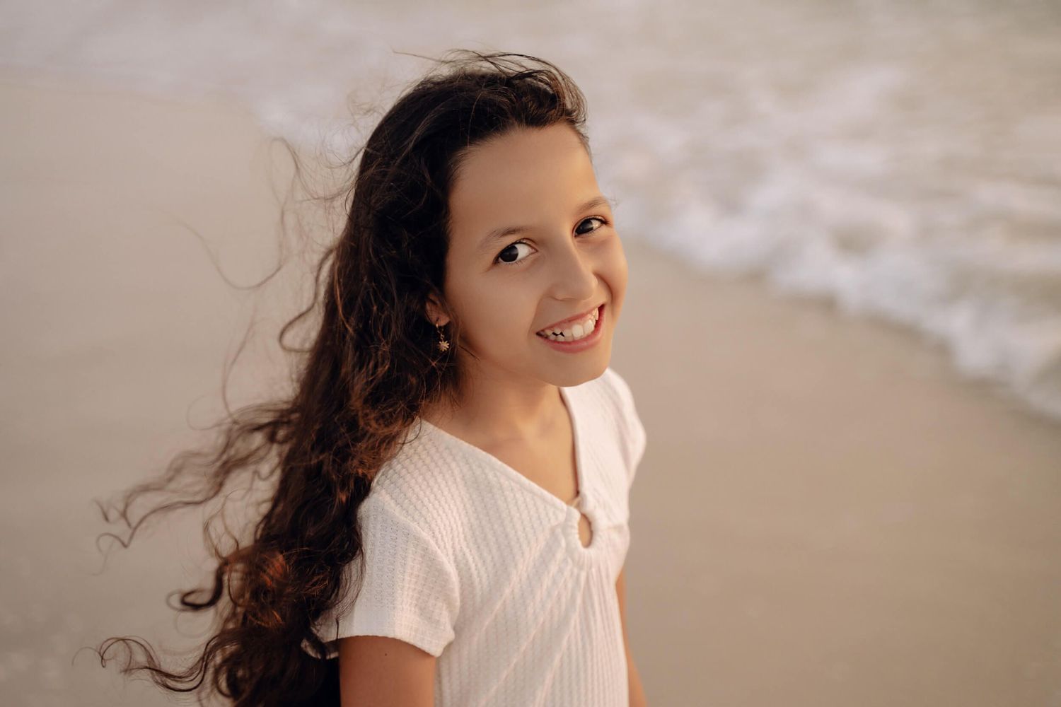 A beaming smile lights up the beach scene as waves crash in the background.