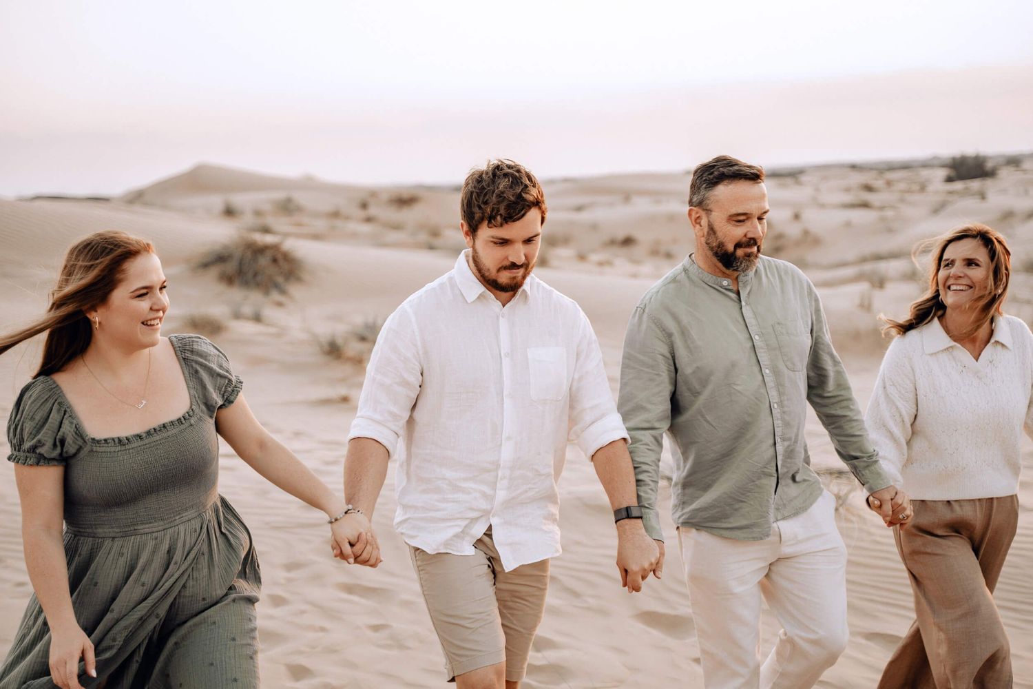 Group holding hands while walking through desert landscape in coordinated casual outfits.