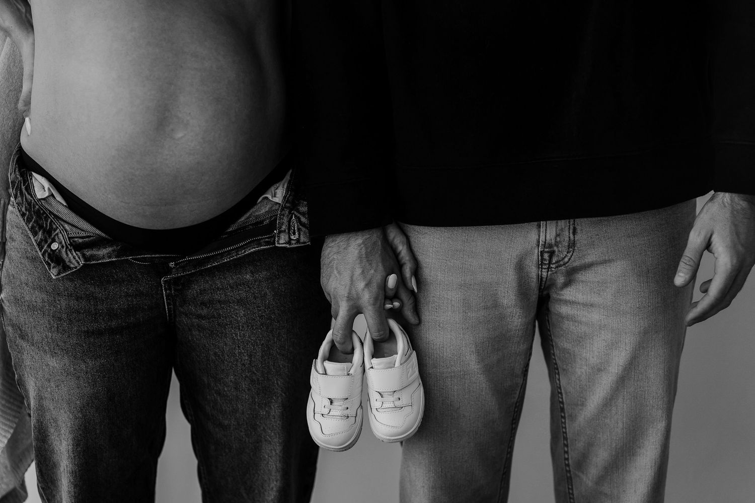 Black and white pregnancy announcement photo featuring baby shoes between two people.