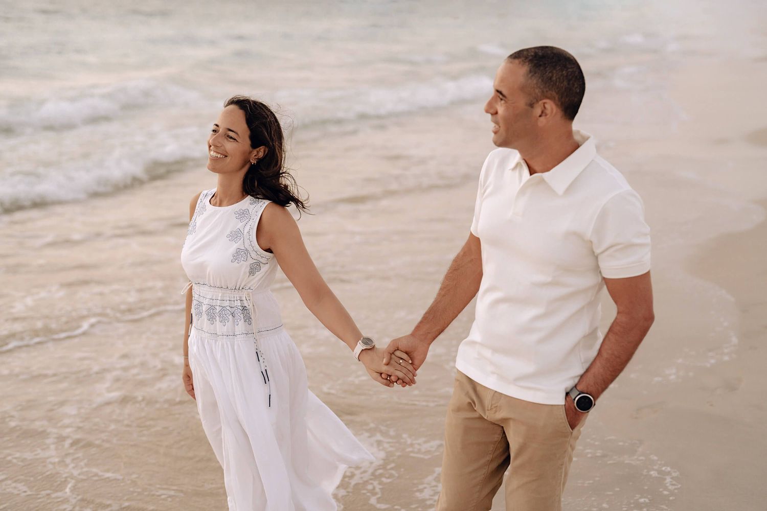 Couple holds hands while enjoying a romantic walk along the beach at sunset.