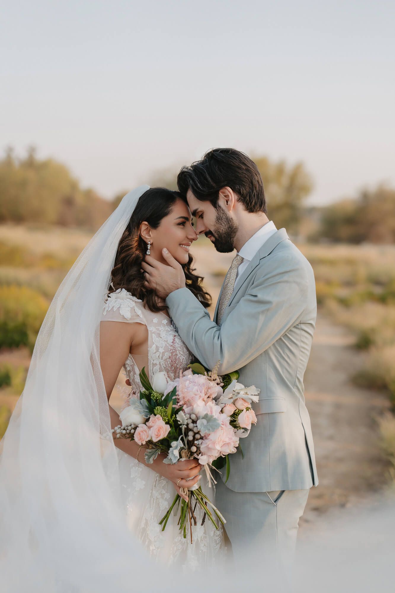 Intimate desert wedding photos showing tender moments between newlyweds with soft pink bouquet at golden hour.