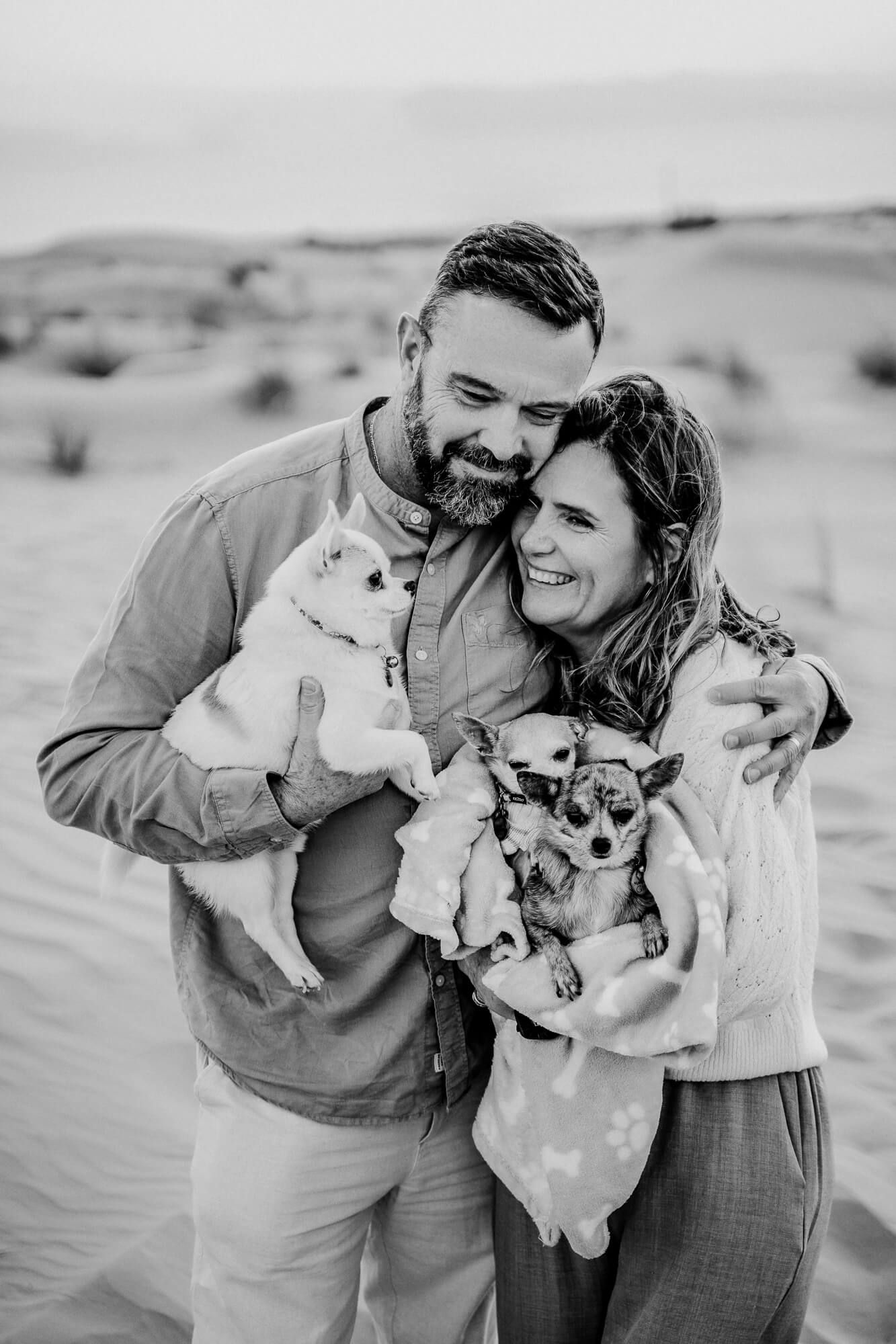 Candid moment of a couple laughing with their chihuahua pet in a desert landscape.