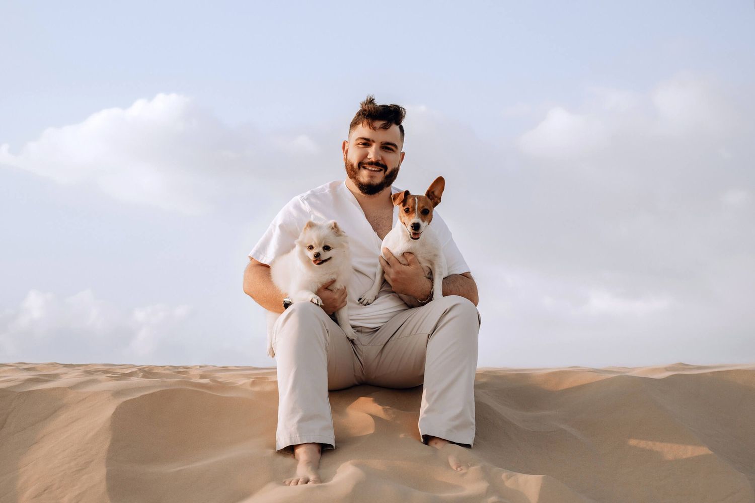 Small dogs sitting together on sandy desert dunes against cloudy sky.
