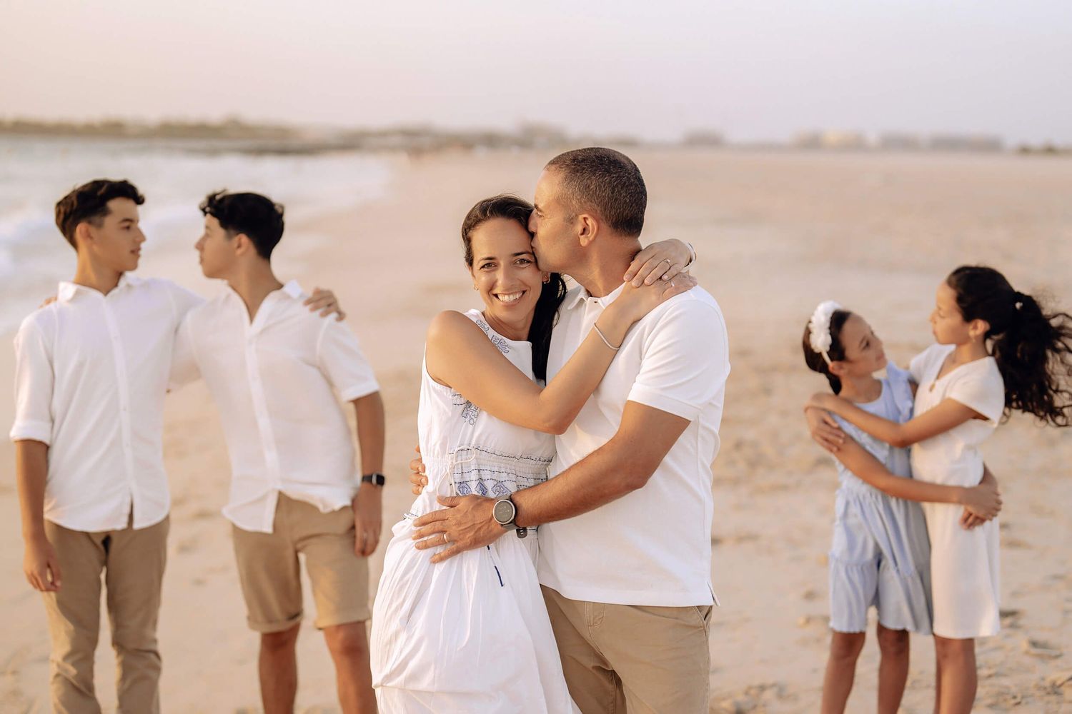 Three couples sharing intimate moments on sandy beach during sunset photoshoot.