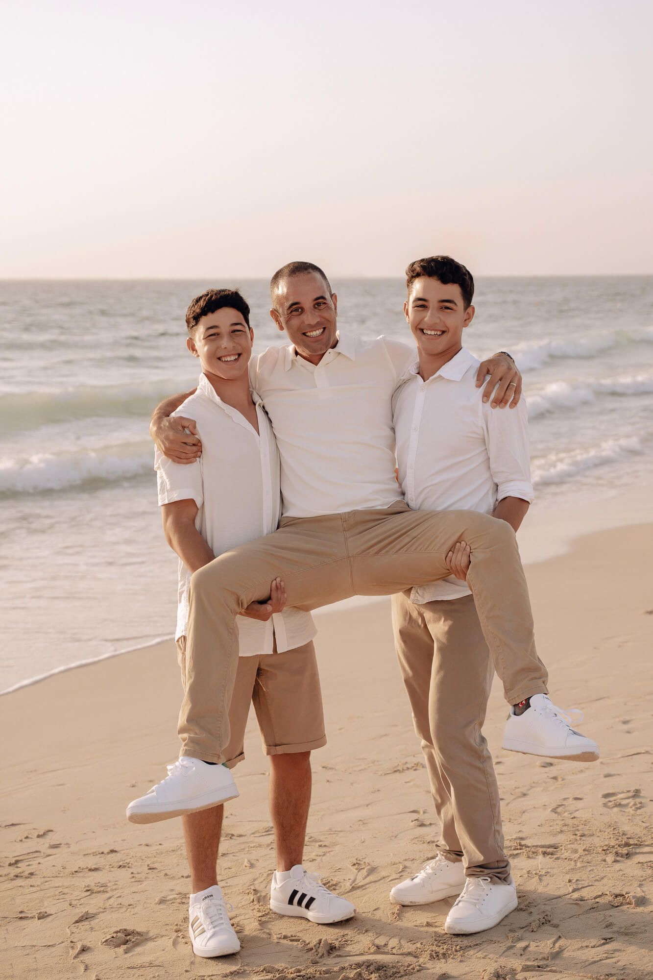 A playful beach photo session showing a coordinated group in white shirts and khaki bottoms at sunset.