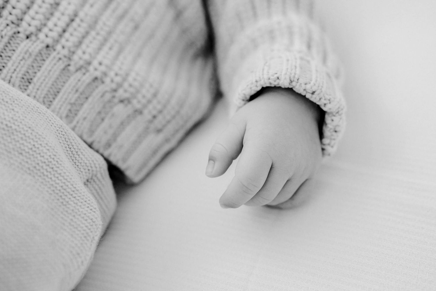 Black and white close-up of a tiny baby hand against white fabric.