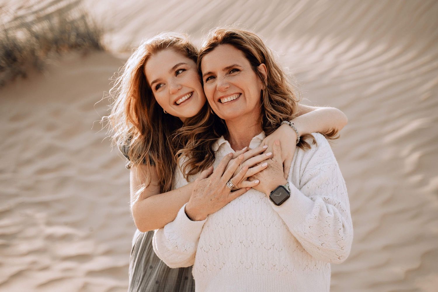 Candid portrait of mother and daughter embracing and laughing against desert backdrop.