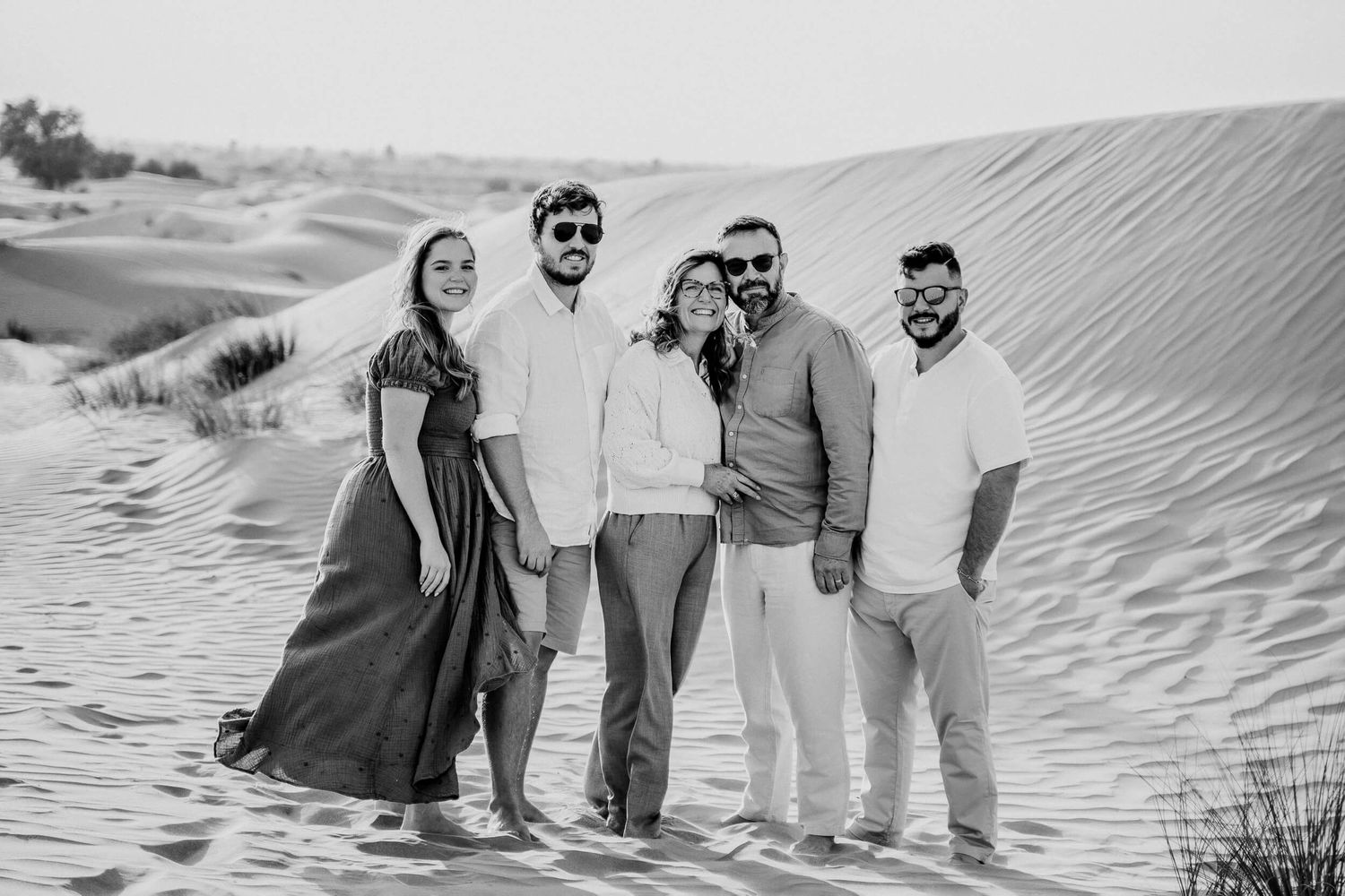 Black and white portrait of five people standing together on desert sand dunes.