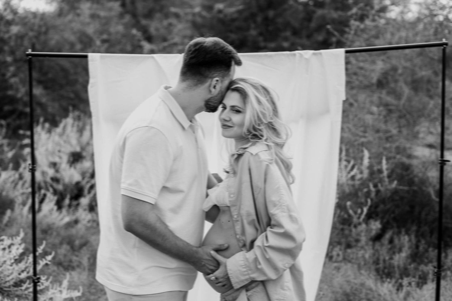 Black and white maternity photo of an expectant couple sharing an intimate moment against a white backdrop.