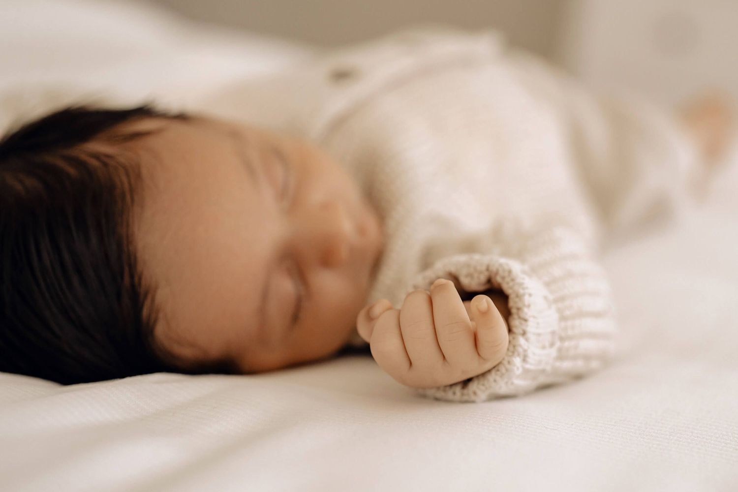Baby sleeping peacefully on white bedding wearing knitted sweater.