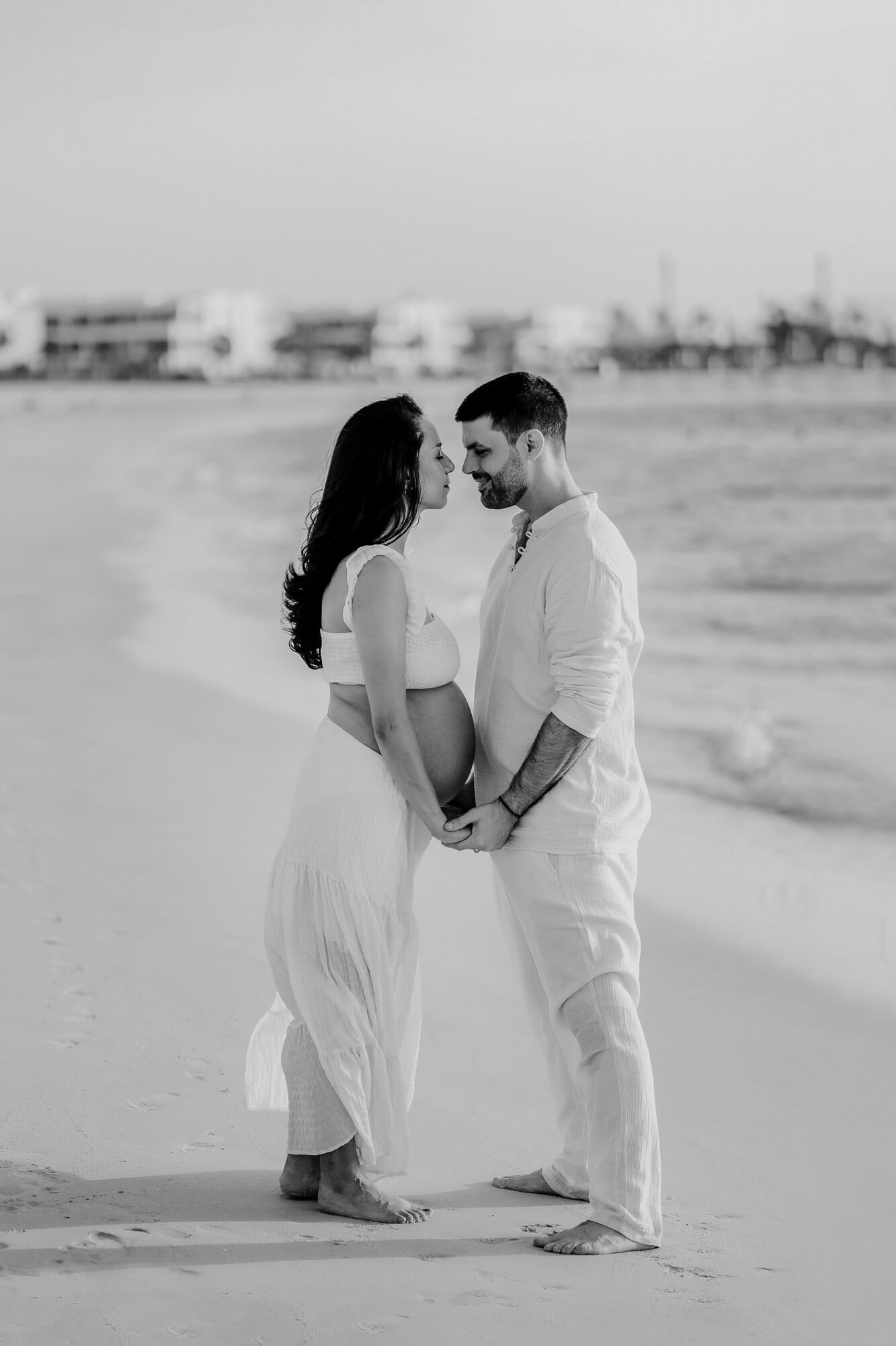 A couple in white attire embracing romantically on a sandy beach in black and white photography.