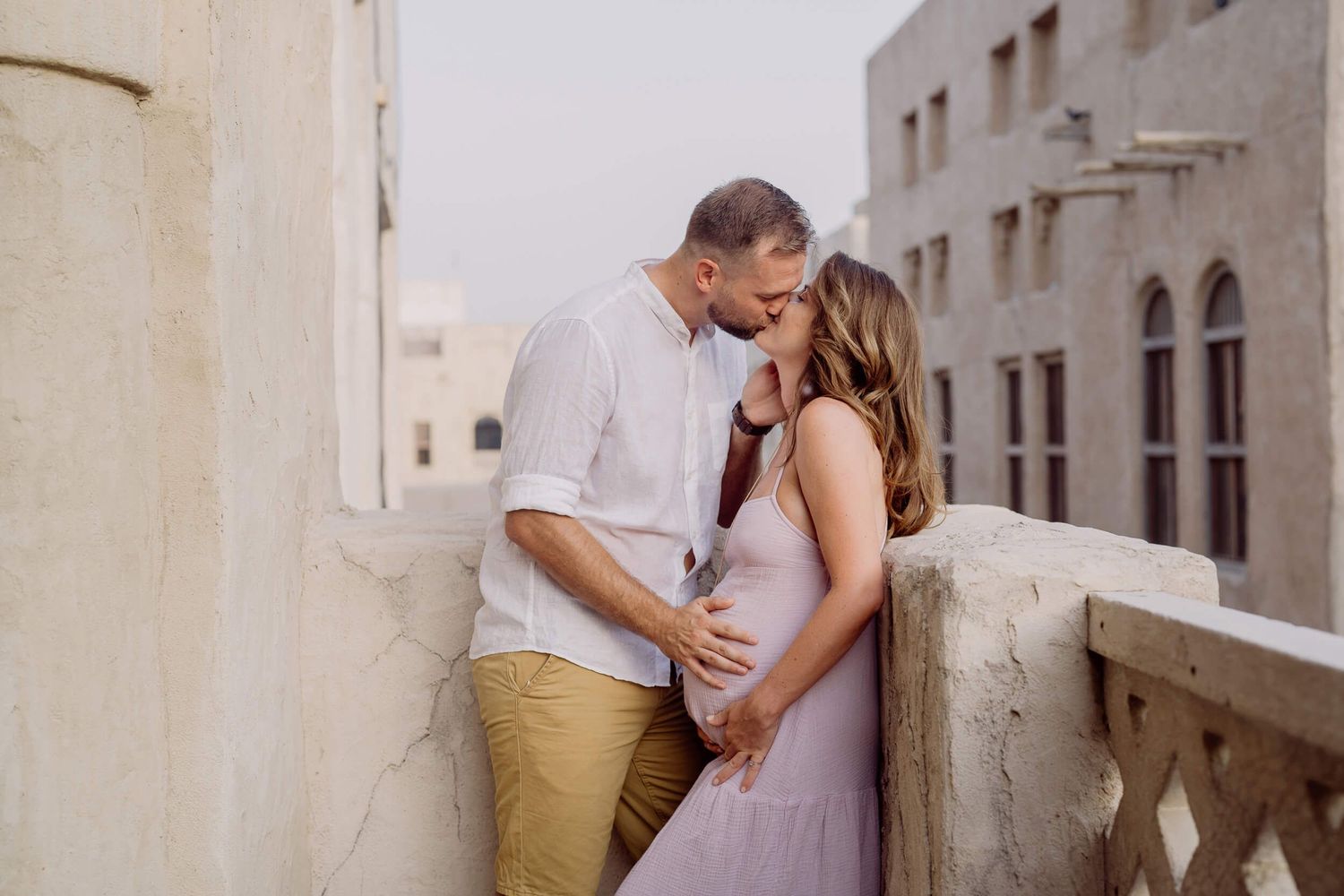 A romantic couple embraces in front of a rustic stone building complex on a sunny afternoon.