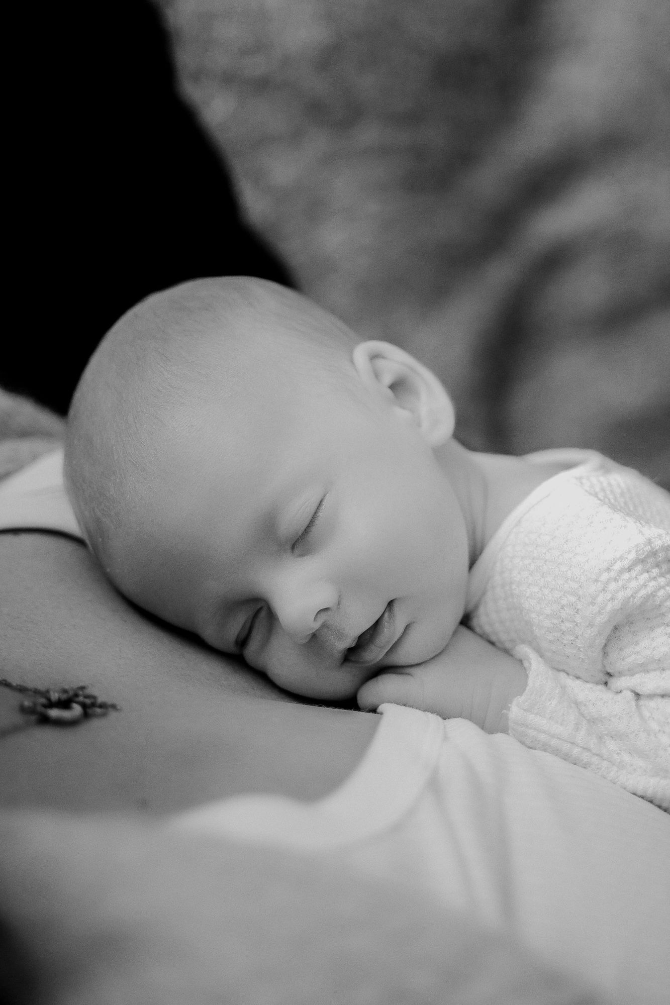 A peaceful black and white portrait of a sleeping newborn baby wearing white clothing and resting on soft fabric.