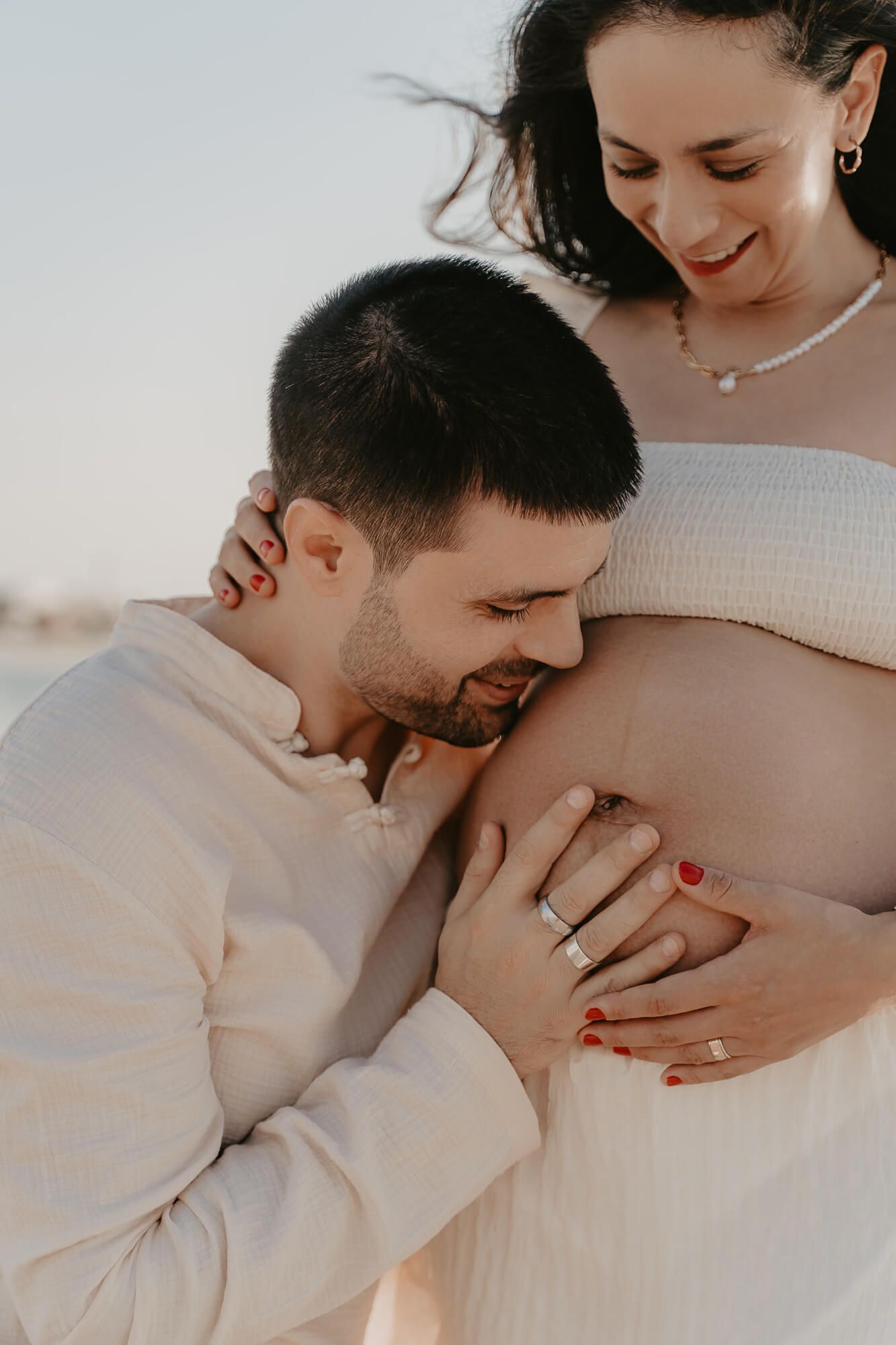 Intimate maternity photo series showing tender moments between expecting parents in soft white attire.