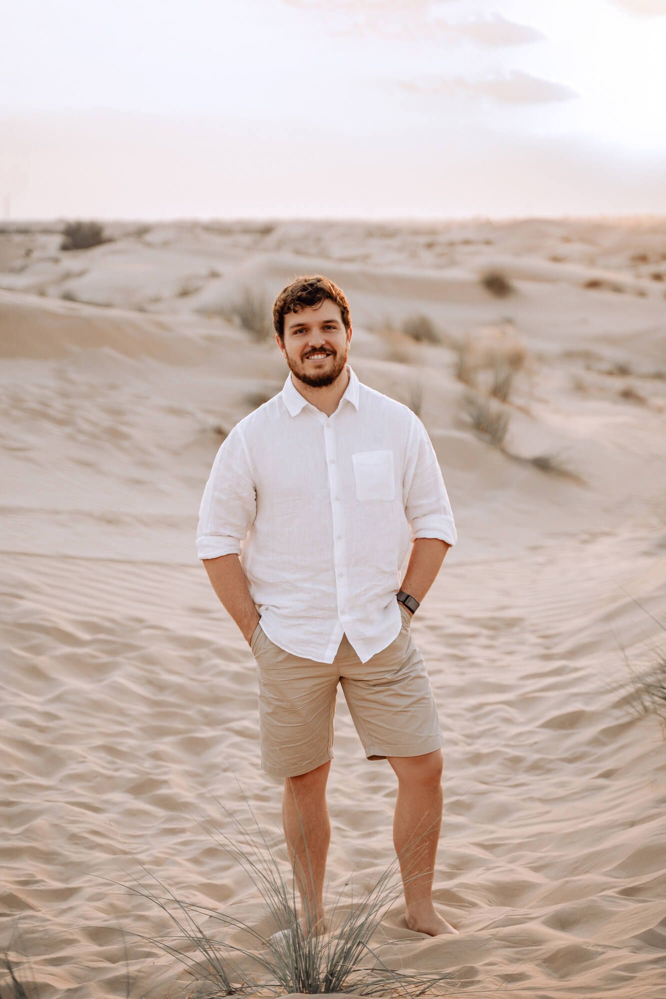 Person in casual white shirt and khaki shorts poses confidently on desert sand dune.