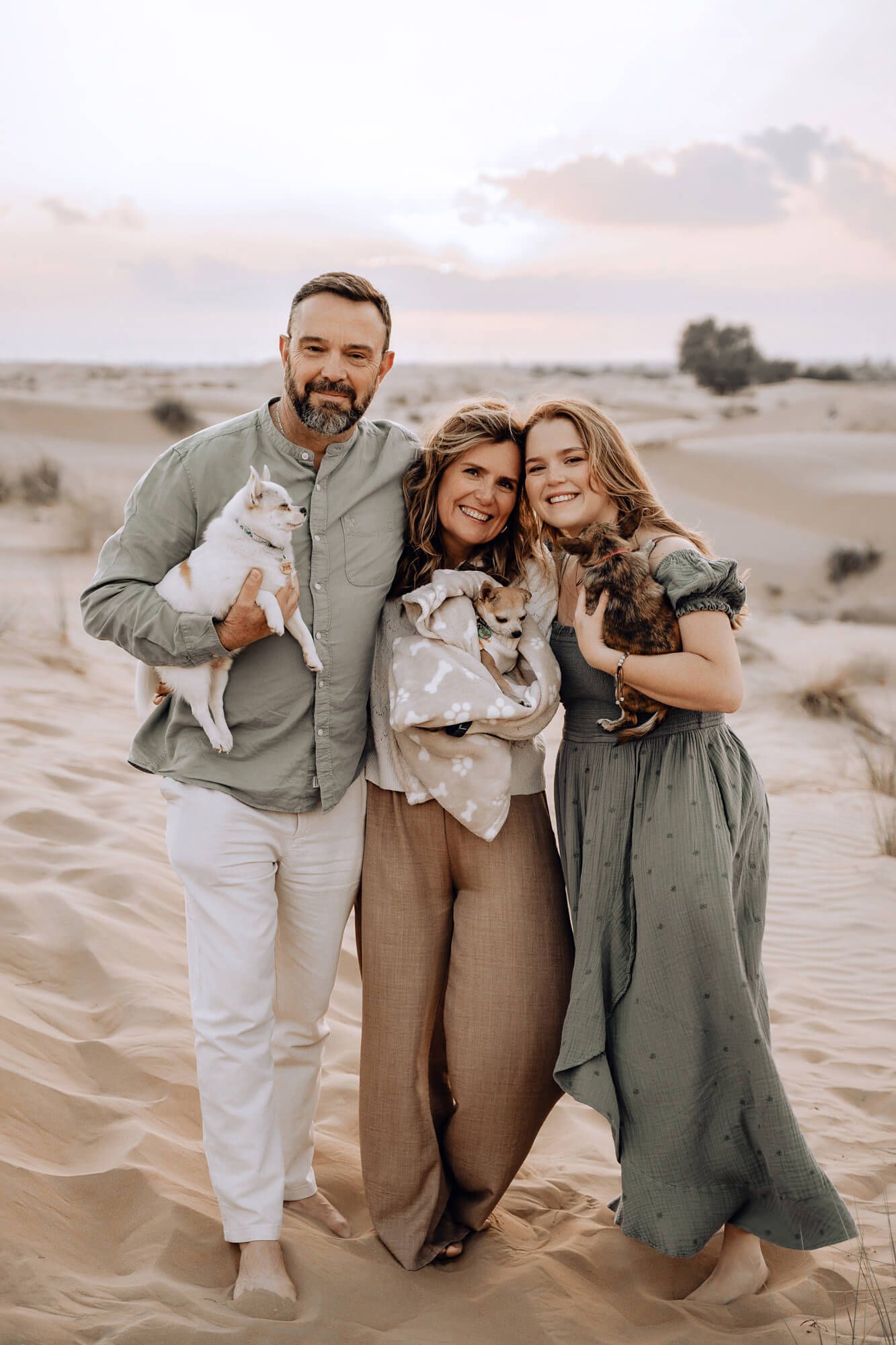Family poses together with their pet chihuahua in a desert setting at sunset.