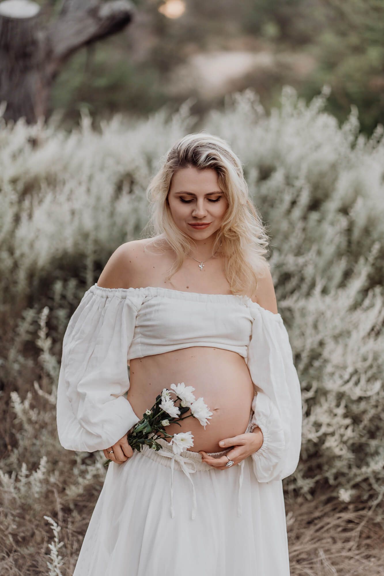 Artistic maternity portrait featuring flowing white dress and flowers in golden afternoon light.