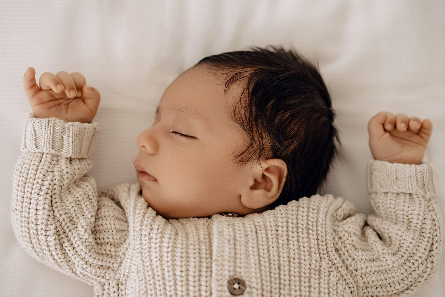 Side profile of sleeping infant in cream sweater against white background.