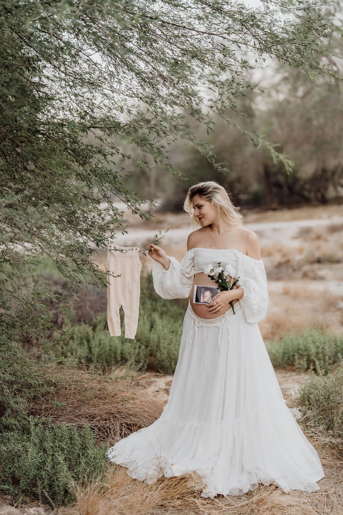 Ethereal outdoor maternity shoot featuring flowing white dress and natural desert landscape.