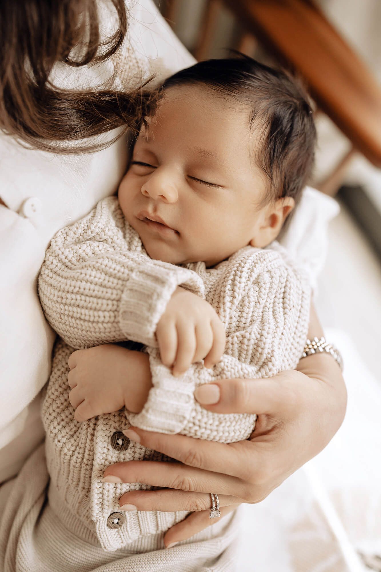 Sleeping newborn wearing knit cardigan rests peacefully in loving embrace.