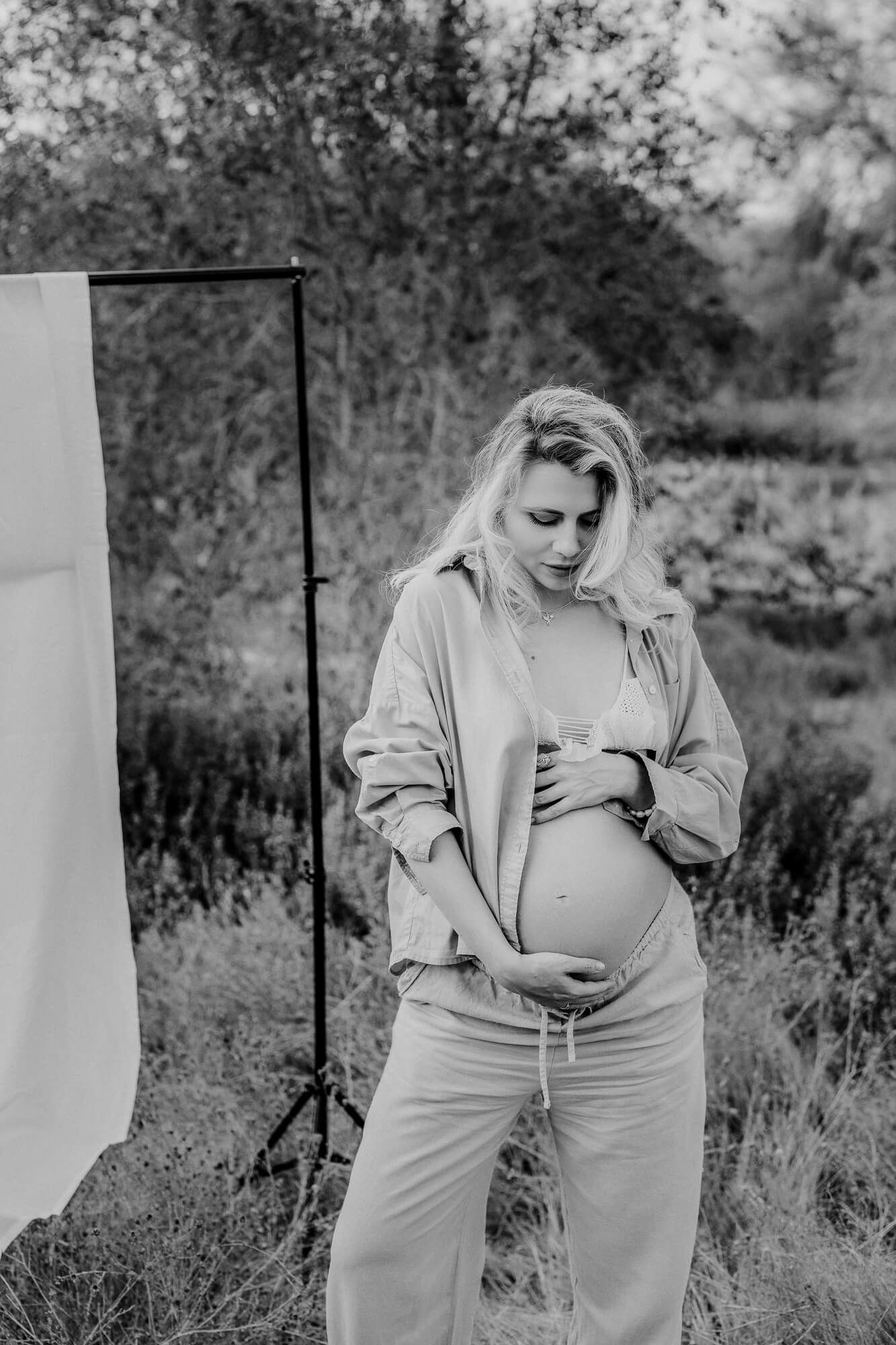 Black and white maternity photos showing pregnant woman posing outdoors against white backdrop.