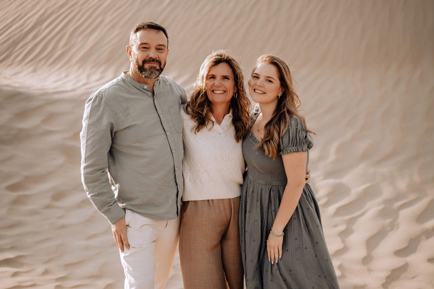 Three people in coordinated outfits posing together against textured sand dune background.