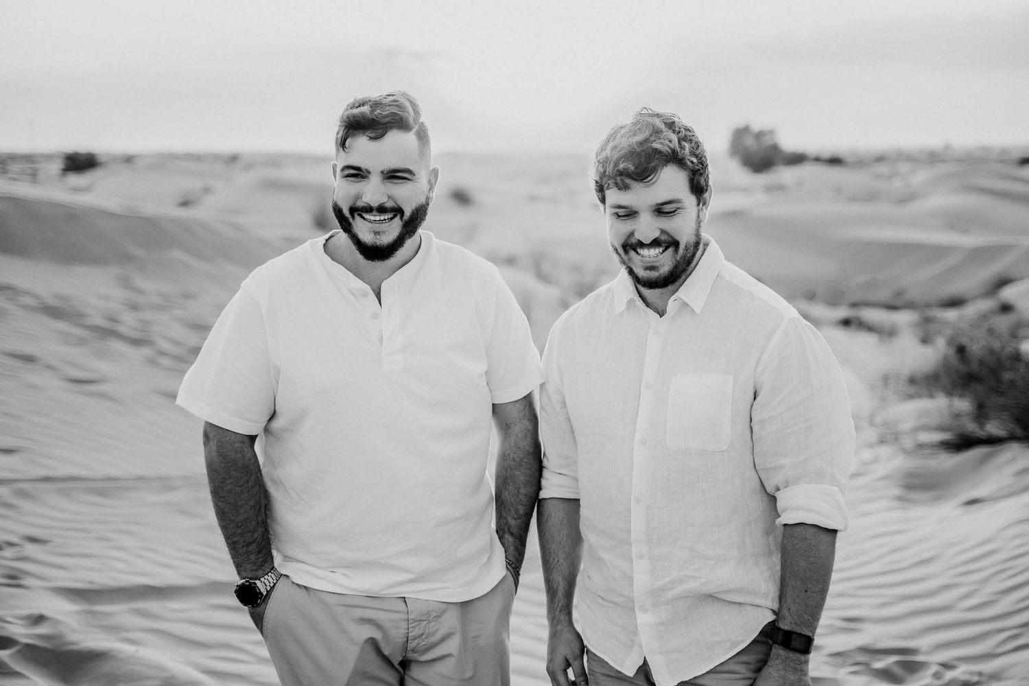 Black and white photo of two people in white shirts standing on sand dunes.