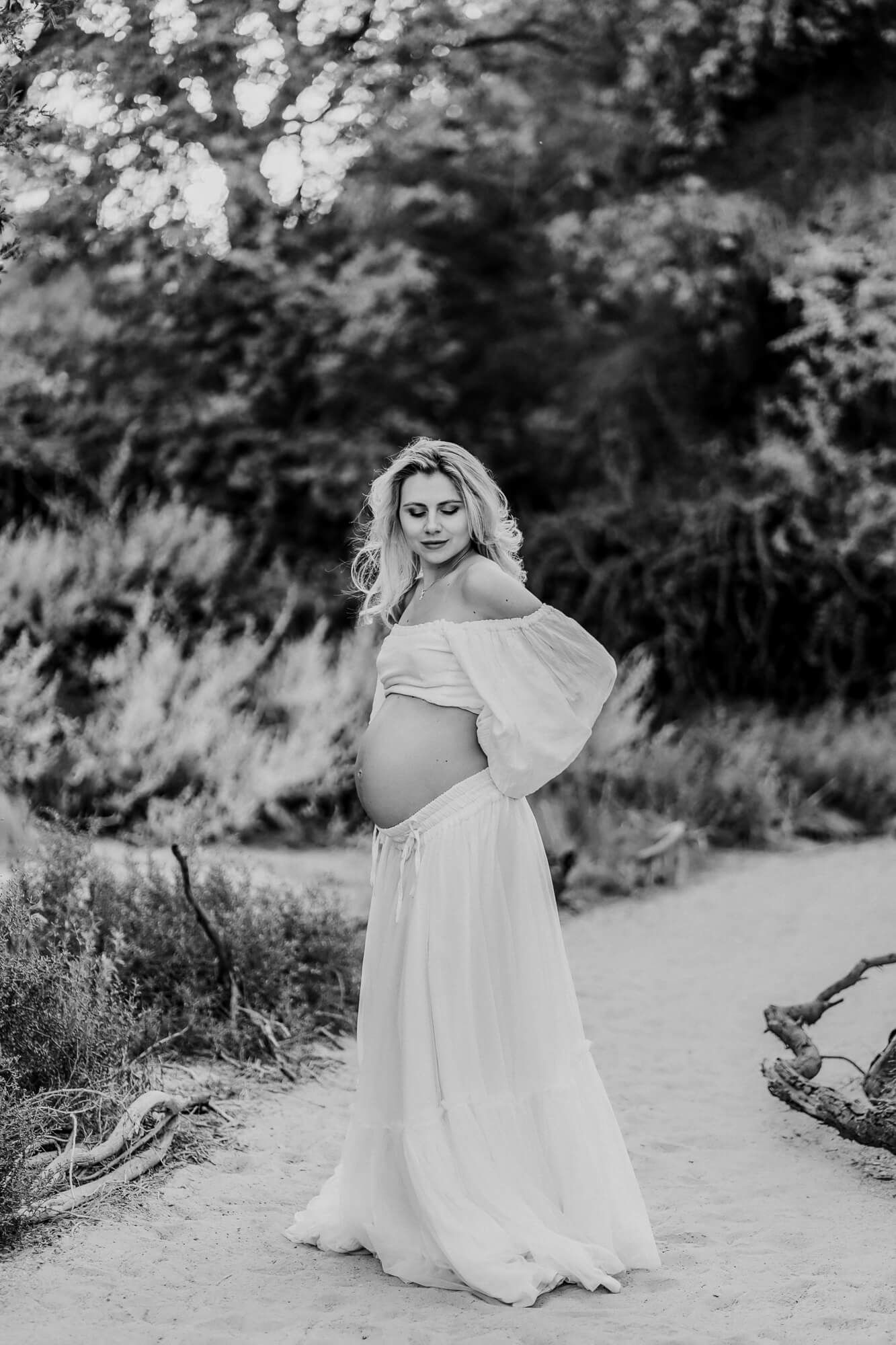 A black and white maternity photo showcasing an elegant pose on a rustic path.