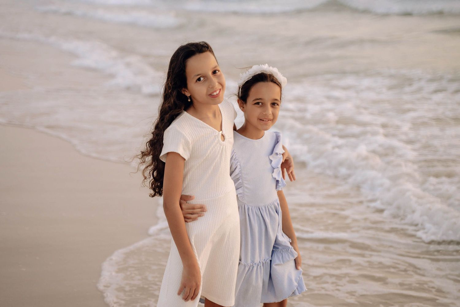 Two people in dresses share a sweet moment together on the beach at sunset.