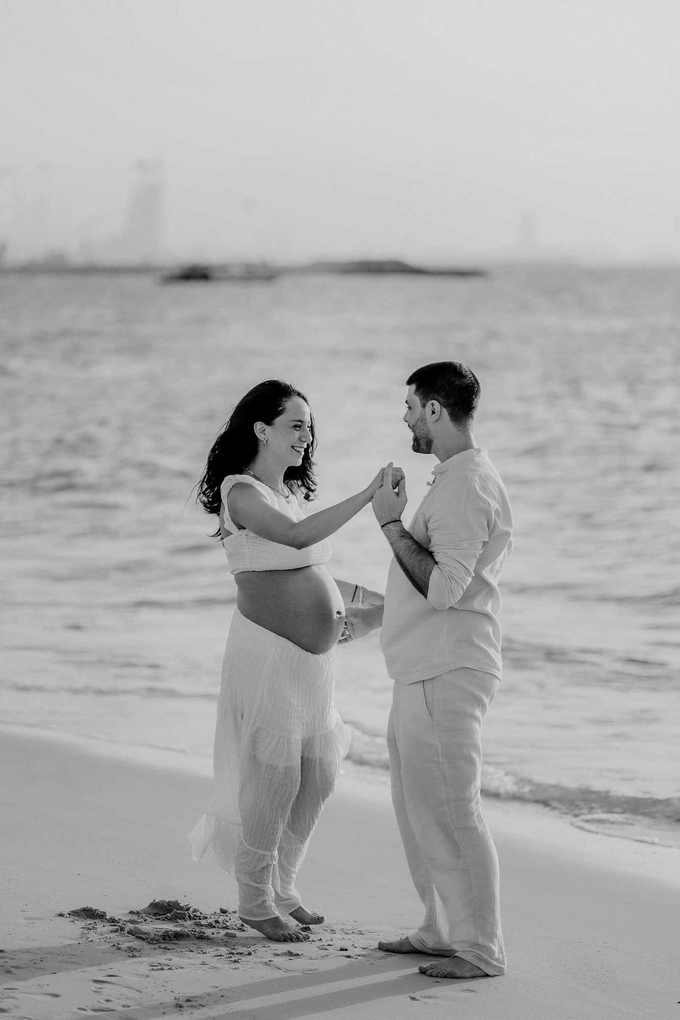 Black and white photo of an intimate maternity moment between a couple on a peaceful beach.