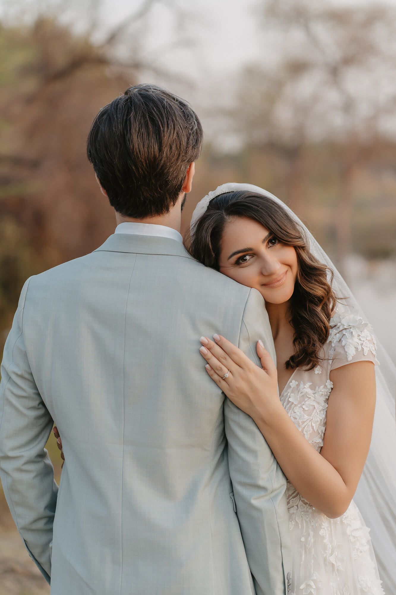 A romantic wedding portrait shows a couple embracing outdoors, with the bride in lace and groom in light gray suit.
