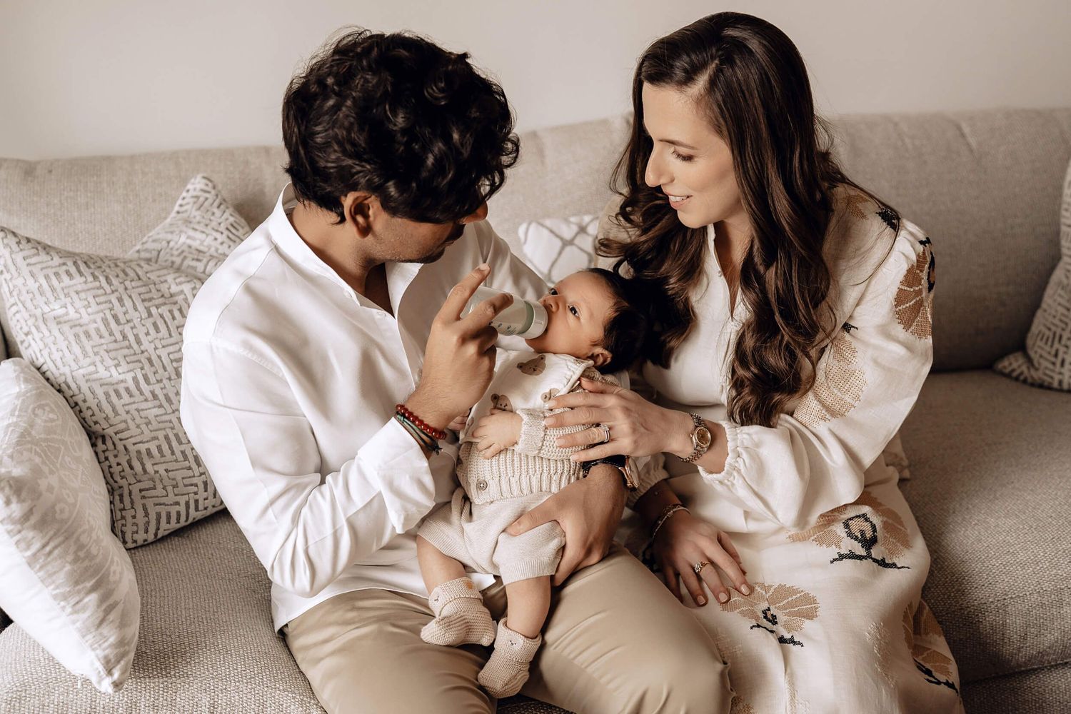 Intimate family photo session showing tender moments with a baby on a couch wearing neutral tones.
