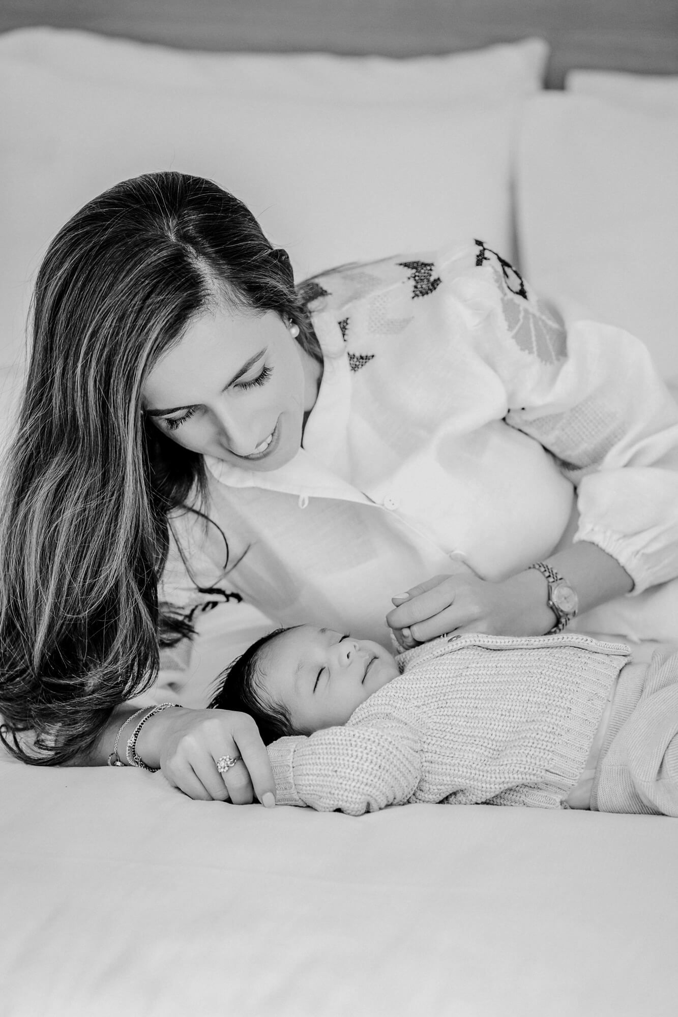 Black and white capture of parent and baby sharing an intimate moment on bedding.