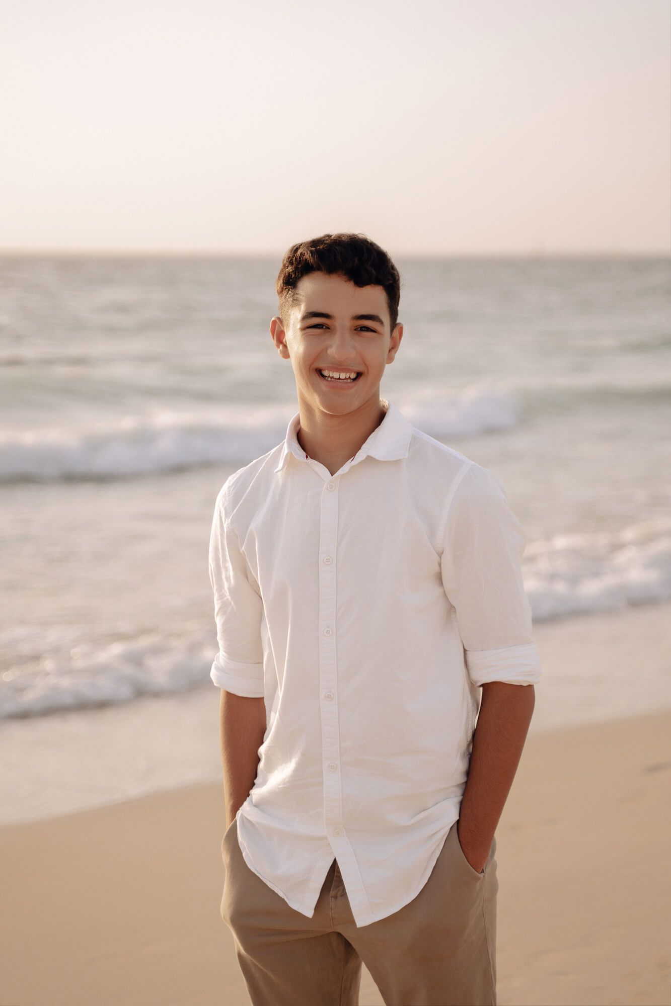 Portrait of someone in white polo shirt and khaki pants on sandy beach at sunset.