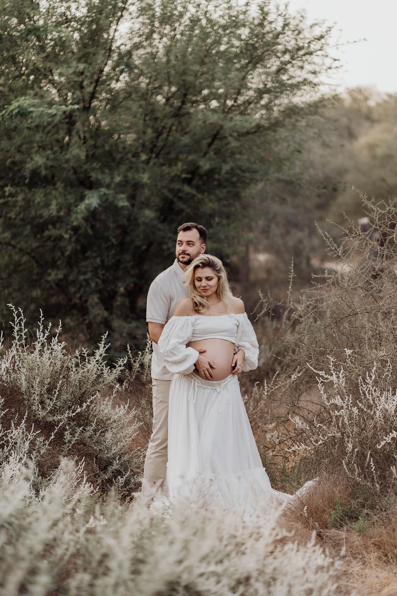 Romantic maternity photography session showing a couple embracing in a desert landscape.