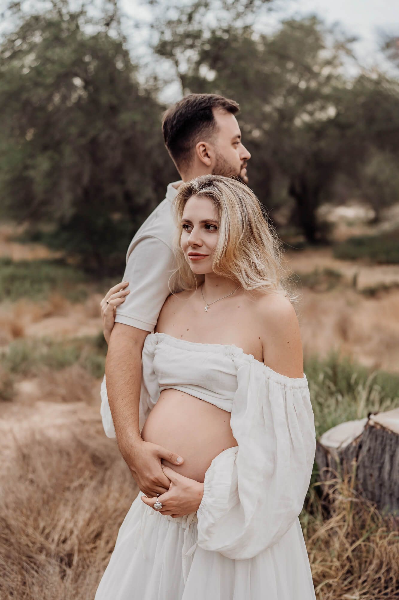 Tender outdoor maternity photography session featuring couple in coordinated white outfits.