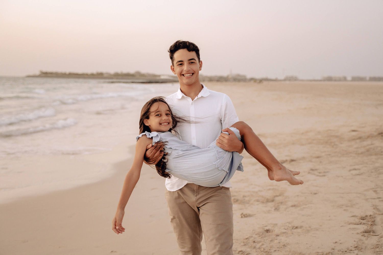 Person carrying another person while smiling on beach during sunset.
