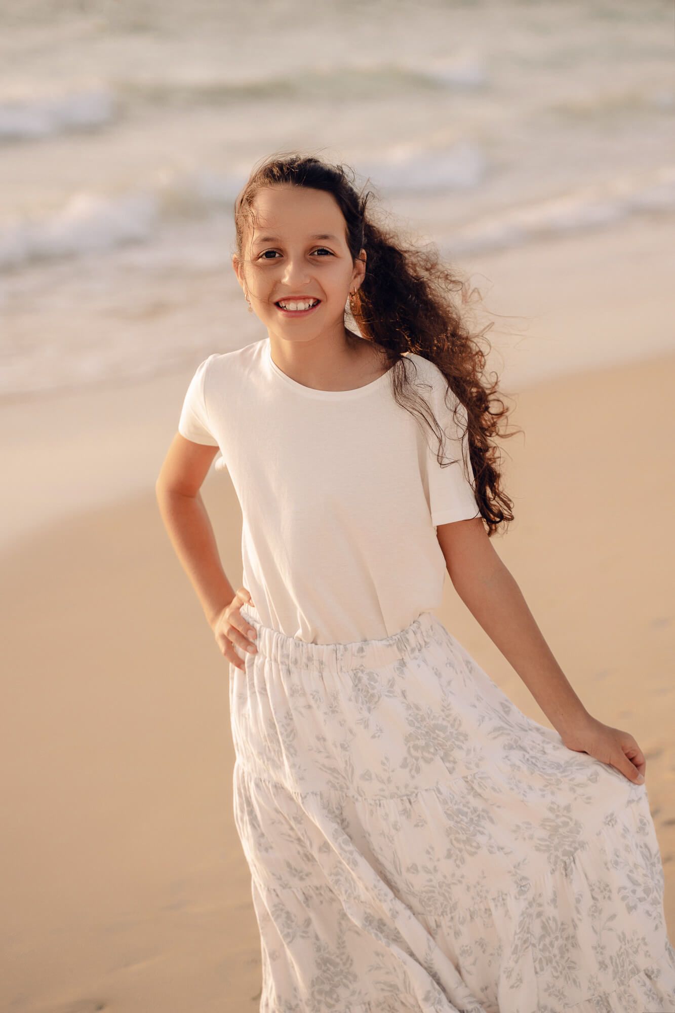 A child's joyful movement captured in a white dress against the sandy beach backdrop.