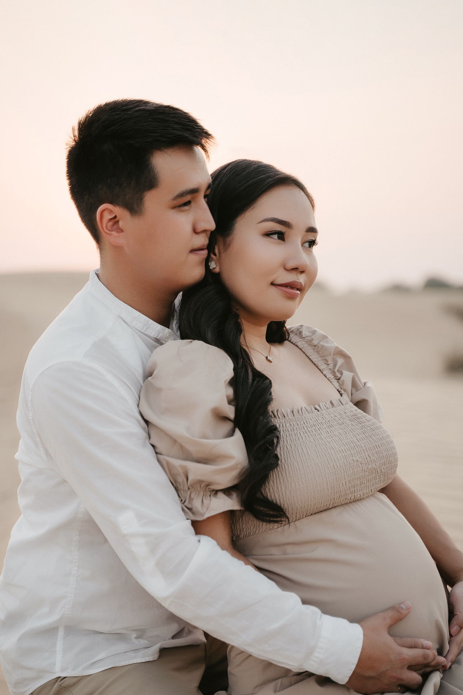 Intimate desert photoshoot featuring couple in neutral tones sharing tender moments on sandy terrain.