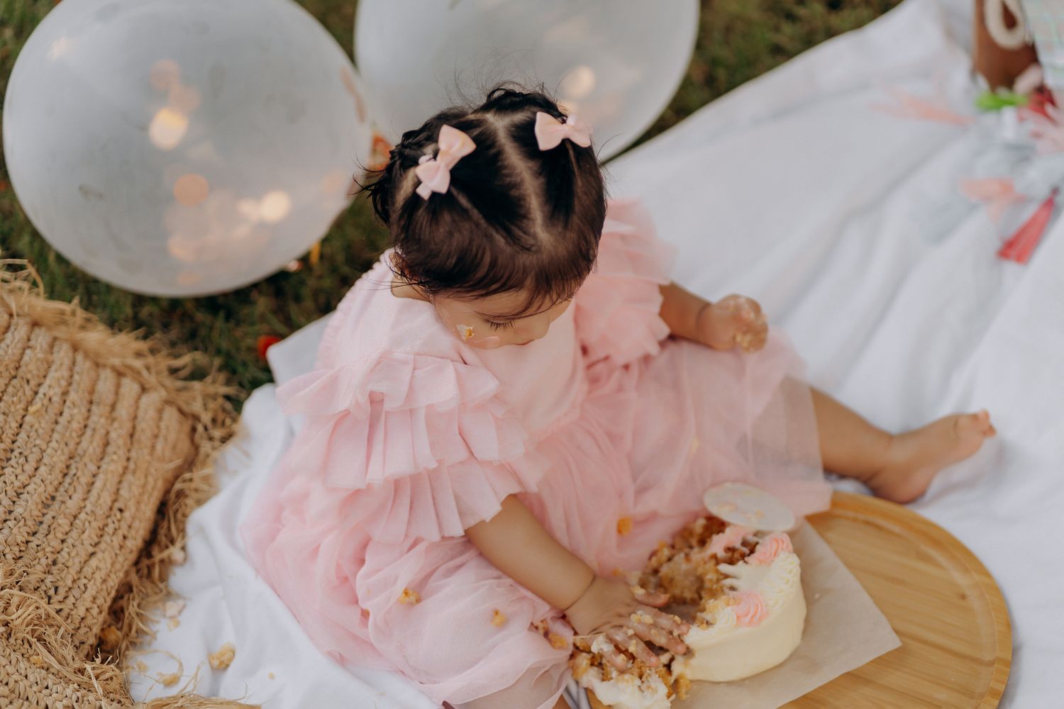 Small child in a pink dress is blowing a bubble during a garden photoshoot.